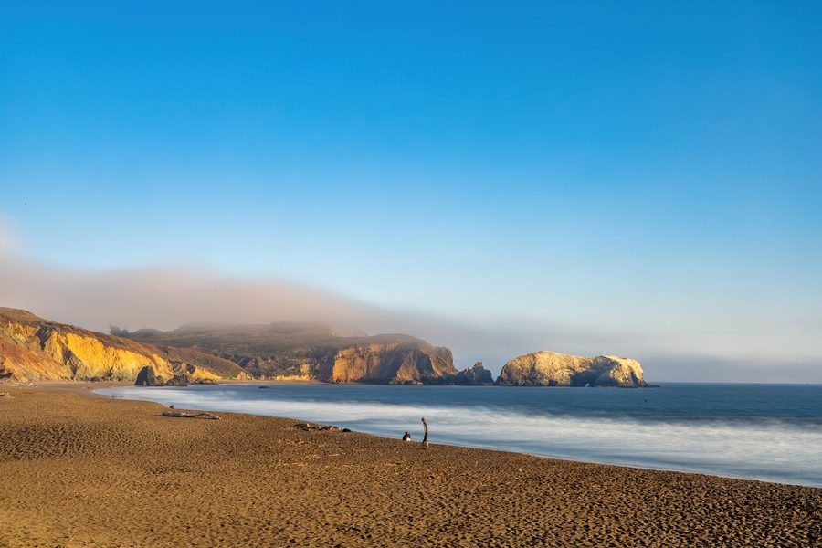 A wide sandy beach with sea stacks and fog rolling over the headland at Goat Rock, Sonoma Coast.