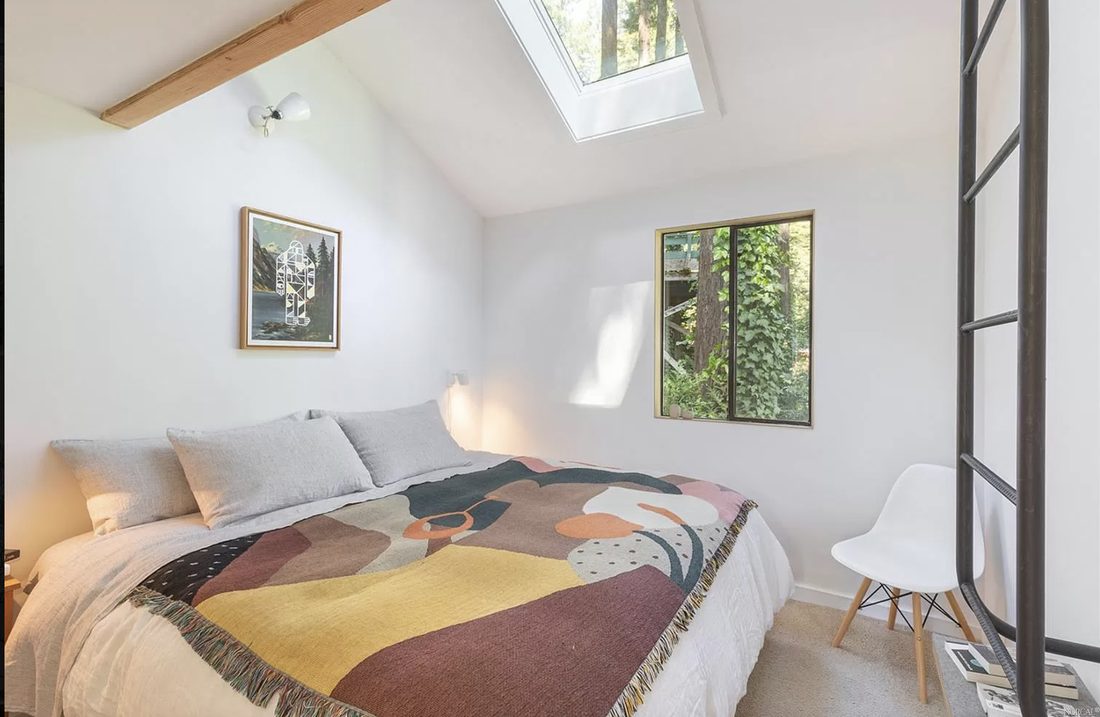 A peaceful bedroom under a sloped ceiling with a skylight and a graphic woven throw.