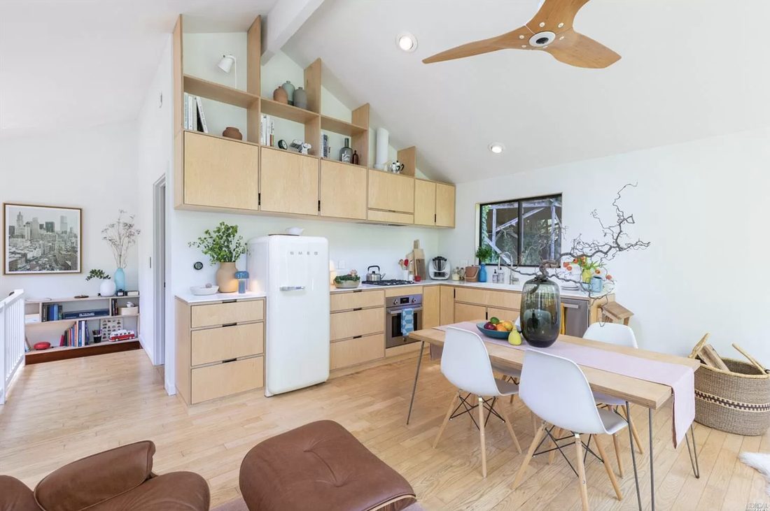 A compact, warm-wood kitchen with open shelving and a window over the sink looking into the trees.